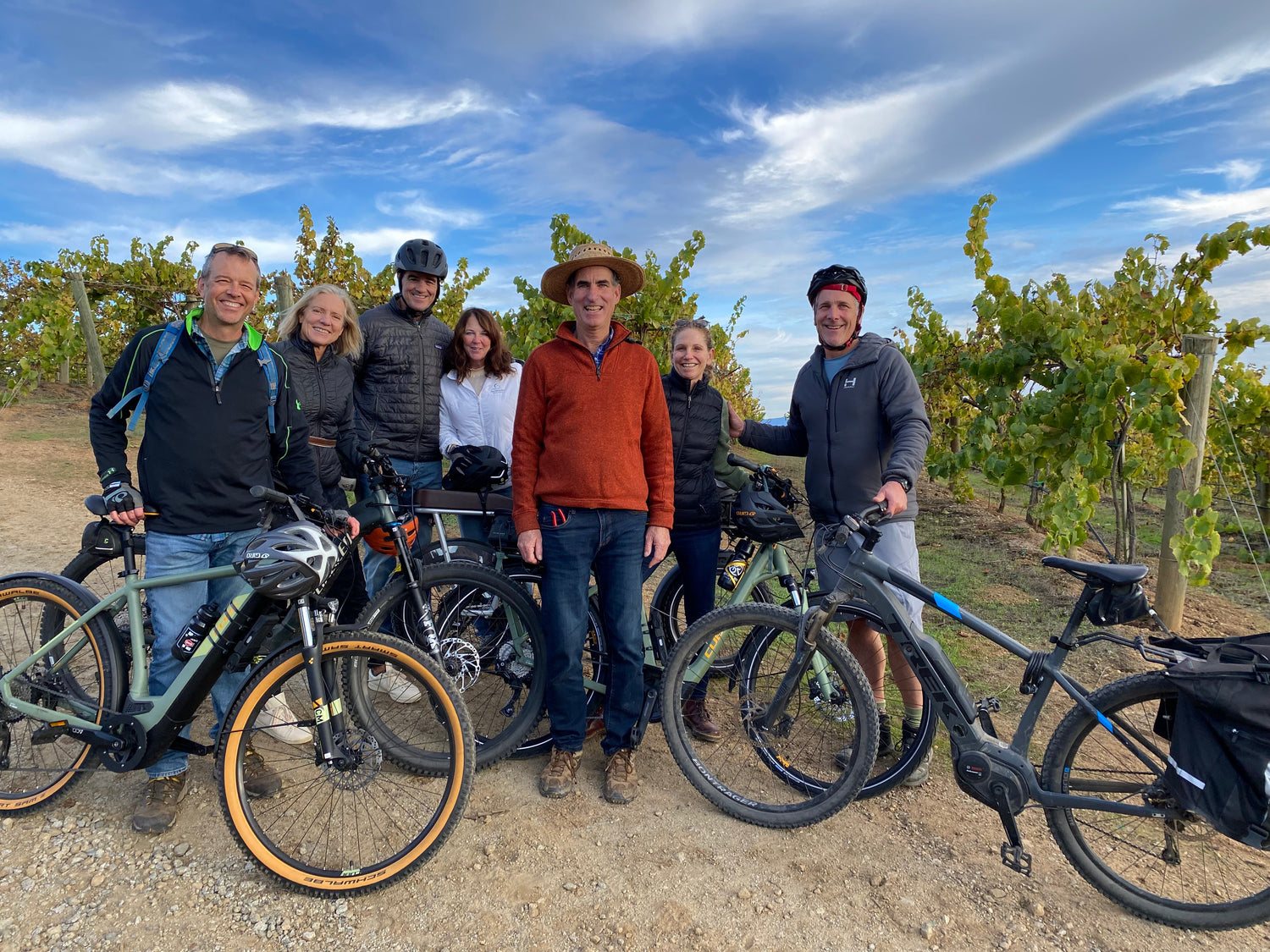 Group of people with bikes standing in a vineyard and smiling.